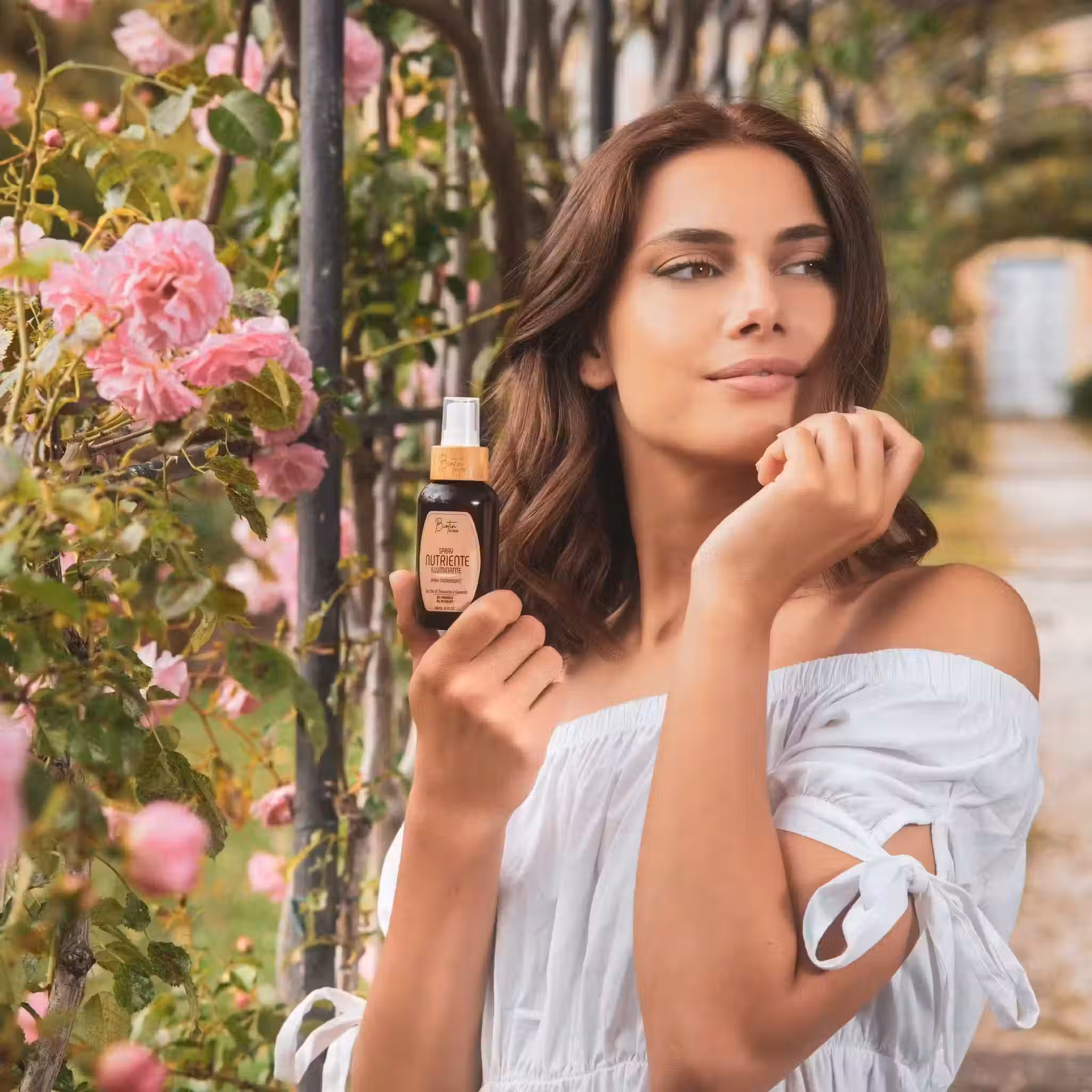 Modella con flacone cosmetico tra fiori rosa